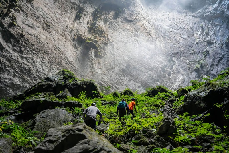 Trekkers on a Son Doong cave trek walking beneath a giant doline with jungle inside the cave