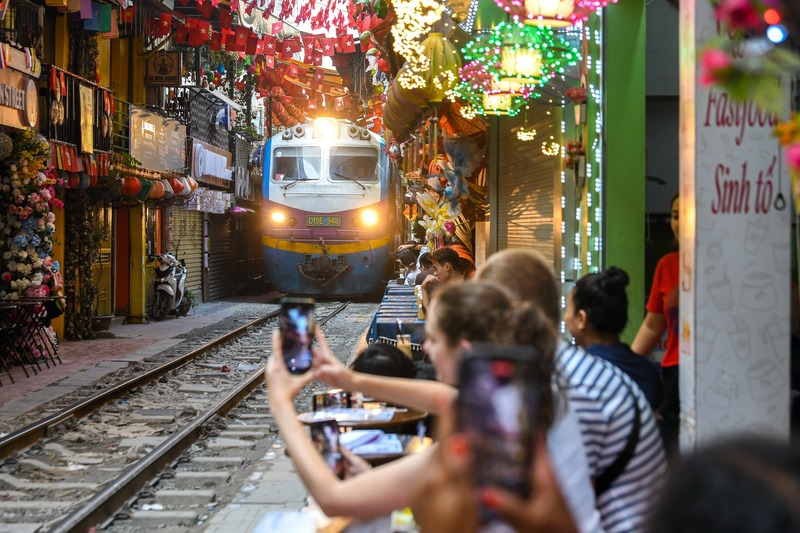 Visitors enjoying coffee at Hanoi Railway Cafe as a train passes through the narrow street